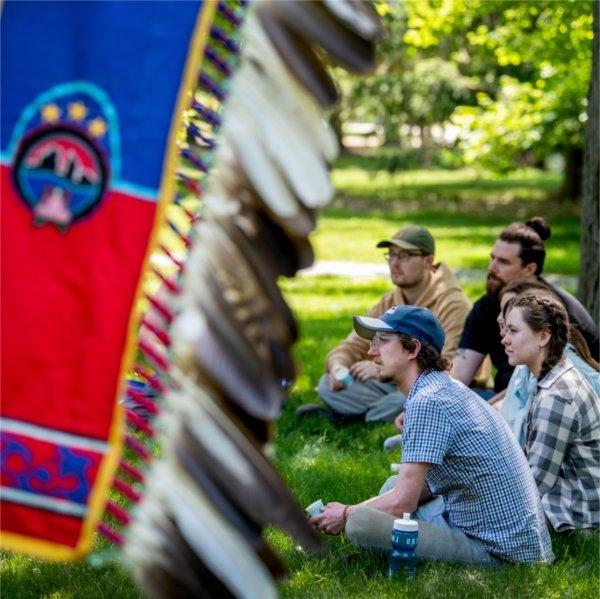 students sit in circle, Native banner with feathers at right